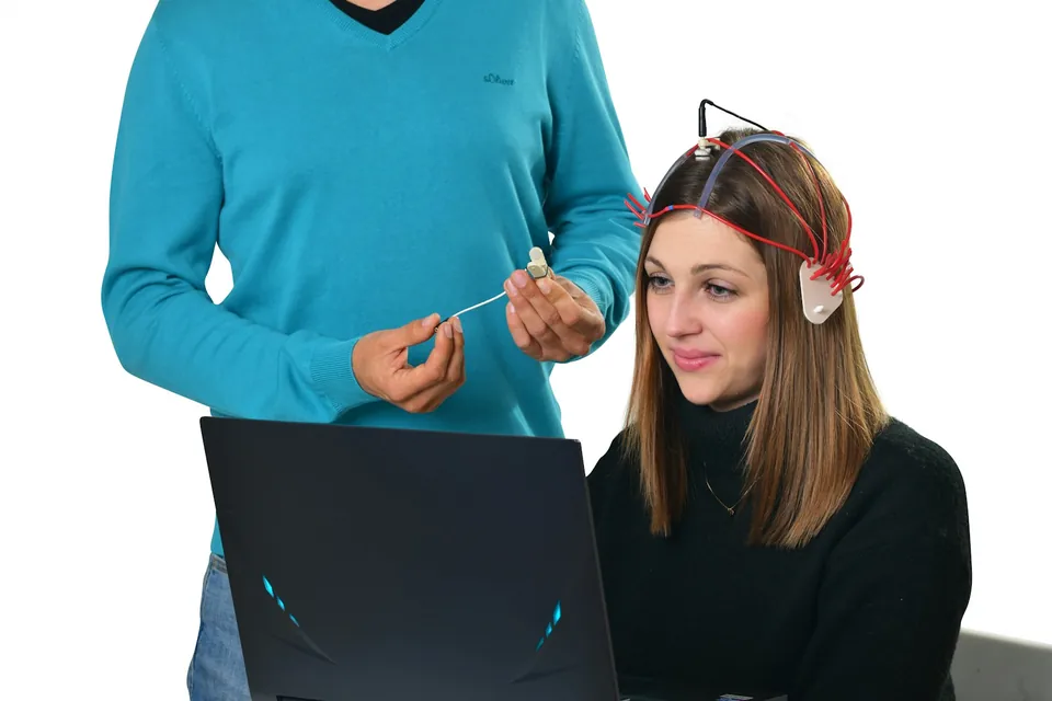 Pessoa com sensores de EEG conectados a um computador, acompanhada por um profissional
